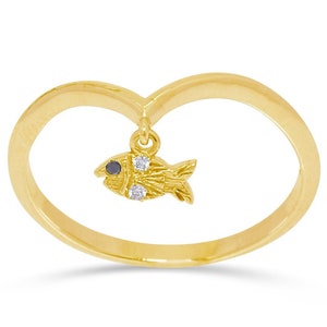Puede incluir: Un anillo de oro en forma de corazón con un colgante de pez. El pez tiene un ojo negro y detalles blancos.