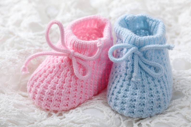 May include: A pair of knitted baby booties, one pink and one blue, with a white lace background.