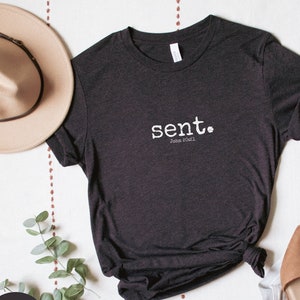 May include: A black heather t-shirt with the word "sent" in white text and the scripture reference "John 20:21" underneath.