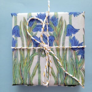 Shown above: A small gift box wrapped in the paper. The box is tied with white twine with a gold thread running through it.