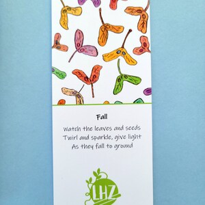 May include: A rectangular card with a white background features colorful watercolor illustrations of falling seeds in shades of orange, yellow, purple, and green. The word "Fall" is printed above a poem. The card also includes a logo and the name "Lynne Zawada."