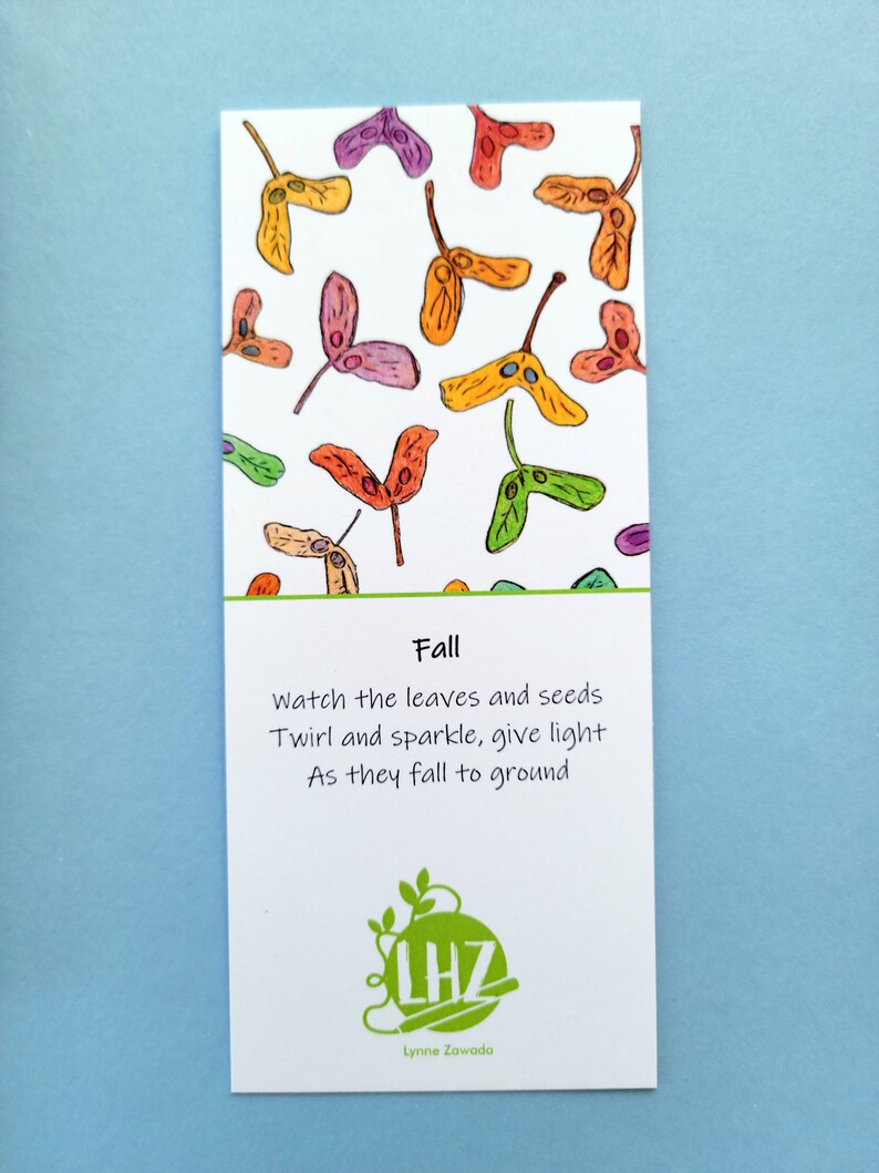 May include: A rectangular card with a white background features colorful watercolor illustrations of falling seeds in shades of orange, yellow, purple, and green. The word "Fall" is printed above a poem. The card also includes a logo and the name "Lynne Zawada."