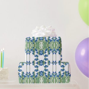 Shown above: a large rectangular gift box and a smaller square medium sized gift box, both wrapped in the paper. The boxes are stacked on top of each other and topped with a white bow (not included). There is a birthday cake with candles on the far right and two balloons on the far left.