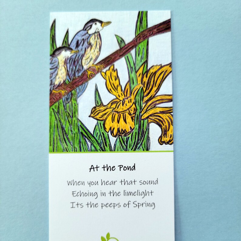 Shown Above: A bookmark with a yellow bog iris and two blue nuthatch birds on a branch. The text on the bookmark reads: "At the Pond, When you hear that sound, Echoing in the limelight, Its the peeps of Spring."