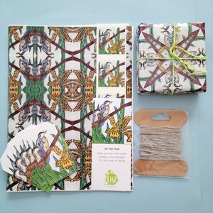 Shown Above: A set of wrapping tissue paper with a repeating pattern of blue birds and iris flowers. The paper is white with green, brown, and yellow accents. The paper is packaged with a matching gift tag and twine. The gift tag has a bird and flower design and the poem "At the Pond, When you hear that sound, Echoing in the limelight, Its the peeps of Spring."