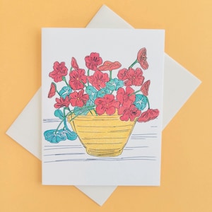 May include: A greeting card featuring a line drawing of a yellow pot filled with red flowers. The flowers are in a simple, stylized design.