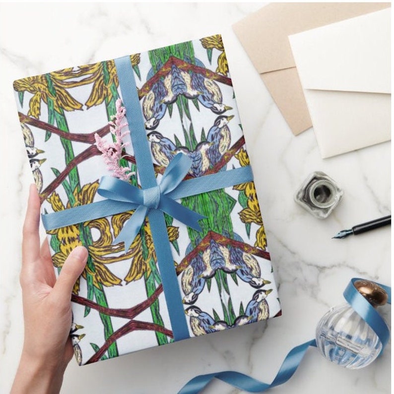 Shown Above: A gift wrapped in the wrapping paper with a blue satin ribbon (not included). The wrapping paper has a repeating pattern of green leaves, yellow flowers, and blue birds. The gift is sitting on a white marble surface.