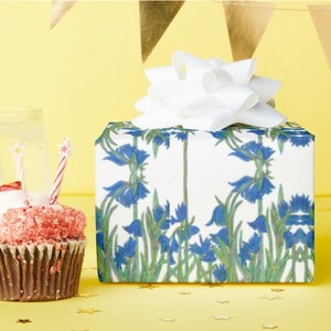 Shown above: A medium sized square gift box with the wrapping, and a white bow on top.  The box is sitting on a yellow surface with gold stars scattered around it and a cupcake with a candle sitting next to it.