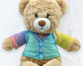 May include: A light brown teddy bear wearing a blue, green, and yellow knitted cardigan. The cardigan has a button closure and a tie-dye pattern.