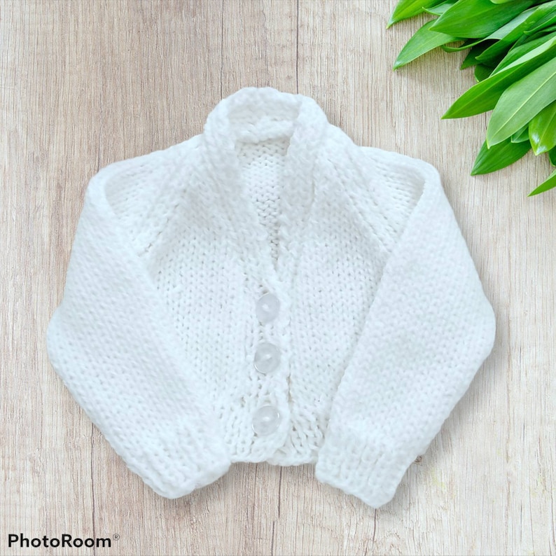 May include: A white knitted cardigan with a button closure. The cardigan has a simple design and is made of a soft, comfortable material.