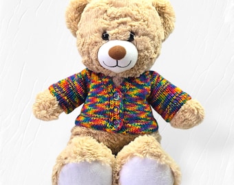 May include: A beige teddy bear wearing a colourful rainbow striped cardigan. The cardigan has a button closure.
