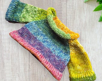 May include: A rainbow striped knitted jumper with a folded collar. The jumper is made with a variety of colours, including green, yellow, orange, blue, purple, and pink.