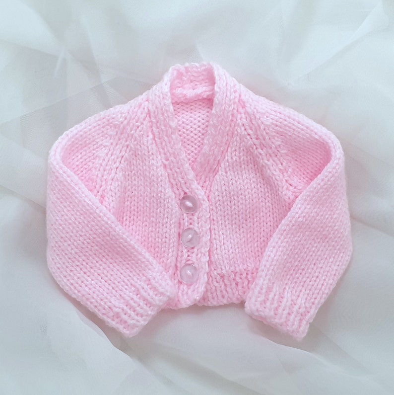 May include: A pink knitted baby cardigan with a button closure.