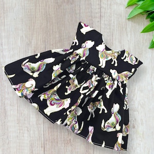 May include: Black dog dress with a white dog pattern. The dogs have colorful paisley designs on their bodies. The dress has a ruffled neckline and a flared skirt, perfect for a pet.