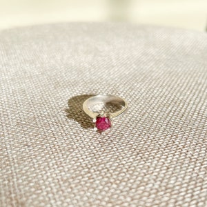 May include: A silver ring with a red gemstone set in a prong setting.