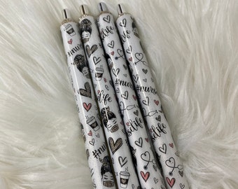 Puede incluir: Cuatro bolígrafos blancos con tinta negra y detalles plateados. Los bolígrafos están decorados con un patrón de corazones, tazas de café y el texto "#nurselife".