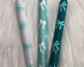 May include: Three glitter pens with white and green bows. The pens are white, light green, and dark green.