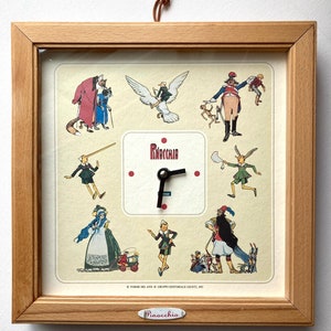 Puede incluir: Un reloj enmarcado en madera con una esfera blanca y agujas negras. La esfera del reloj presenta ilustraciones de la historia de Pinocho, incluyendo al propio Pinocho, Geppetto y el Hada Azul. El reloj está etiquetado como "Pinocchio" en la parte inferior.