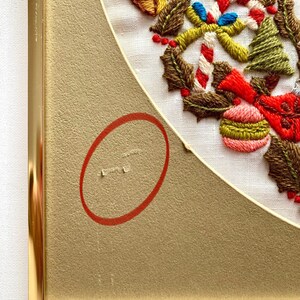 May include: A framed embroidery of a Christmas wreath with holly, candy canes, baubles, and a bell. The wreath is stitched in various colours of thread on white fabric. The frame is gold.