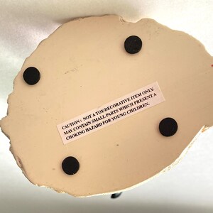 May include: White ceramic figurine with a textured surface. The figurine has four black felt pads on the bottom. The figurine has a warning label that reads: "CAUTION: NOT A TOY-DECORATIVE ITEM ONLY. MAY CONTAIN SMALL PARTS WHICH PRESENT A CHOKING HAZARD FOR YOUNG CHILDREN."