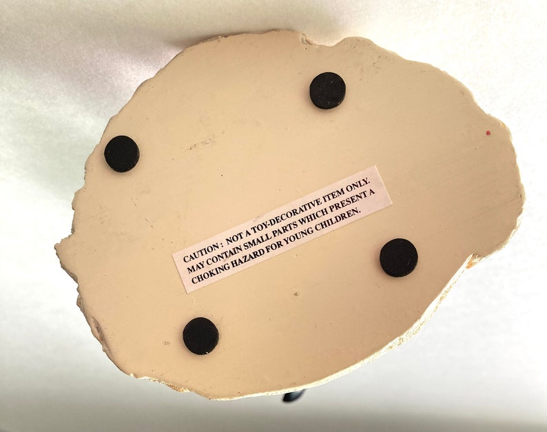 May include: White ceramic figurine with a textured surface. The figurine has four black felt pads on the bottom. The figurine has a warning label that reads: "CAUTION: NOT A TOY-DECORATIVE ITEM ONLY. MAY CONTAIN SMALL PARTS WHICH PRESENT A CHOKING HAZARD FOR YOUNG CHILDREN."