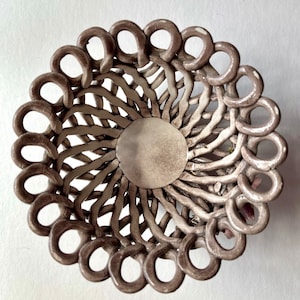 Könnte beinhalten: Eine weiße Keramikschale mit geflochtenem Design. Die Schale ist rund und aus hellem braunen Material gefertigt. Die Schale eignet sich perfekt für die Aufbewahrung von kleinen Gegenständen wie Schmuck oder Nippes.