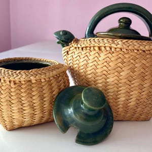 Puede incluir: Un juego de dos teteras o cafeteras de mimbre tejido con tapas de cerámica verde. La tetera más pequeña tiene forma redonda y la más grande tiene un pico.