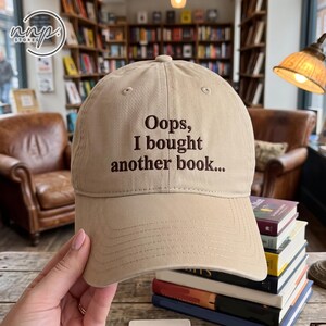 Peut inclure: Une casquette de baseball beige avec le texte brodé en marron foncé "Oops, I bought another book..." sur le panneau avant. La casquette présente une calotte structurée, une visière incurvée et des œillets cousus pour la ventilation.