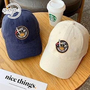 Puede incluir: Dos gorras de béisbol, una azul marino y otra blanquecina, están sobre una mesa de madera. Cada gorra tiene un parche circular con el texto "PROJECT HAIL MARY" y un gráfico. Una taza de Starbucks es visible en el fondo.