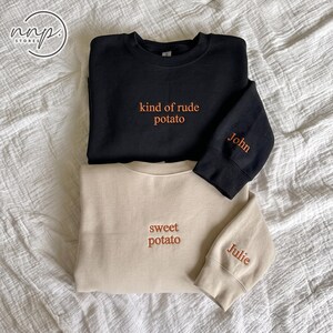 以下が含まれることがあります： kind of rude potatoと刺繍された黒のクルーネックトレーナーの袖にはJohnという名前があり、sweet potatoと刺繍されたベージュのクルーネックトレーナーの袖にはJulieという名前が刺繍されています。