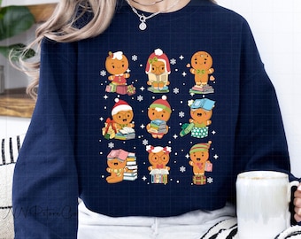 May include: Navy blue sweatshirt featuring a repeating pattern of gingerbread people with books, gifts, and Santa hats. The gingerbread characters are in various poses, surrounded by snowflakes. The sweatshirt is a comfortable, casual style.