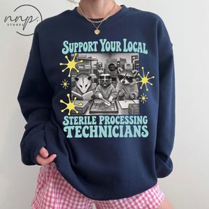 Könnte beinhalten: Ein marineblaues Sweatshirt mit Rundhalsausschnitt und einem Grafikdruck mit dem Text "SUPPORT YOUR LOCAL STERILE PROCESSING TECHNICIANS" in Hellblau. Das Bild zeigt drei Tiere in einem Labor mit gelben Sternakzenten.