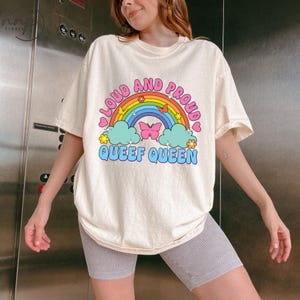 May include: A white t-shirt with a rainbow and the text "Loud and Proud Queef Queen" printed on it.