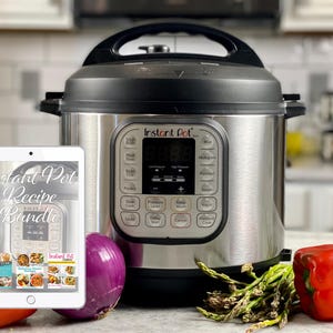 Op de afbeelding: Een zilveren Instant Pot elektrische snelkookpan met een digitaal display en een tablet waarop "Instant Pot Recipe Bundle" staat. De Instant Pot staat op een aanrecht met een rode paprika, een paarse ui en groene asperges.
