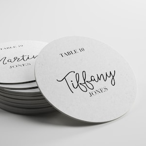 May include: White round table number card with black text. The card says "TABLE 10" and "Tiffany JONES".