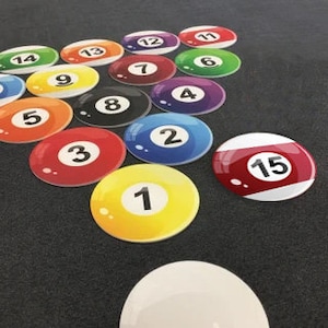 May include: A set of 15 billiard balls in a triangle formation on a green felt pool table. The balls are numbered 1 through 15, with the 8 ball in the center. The cue ball is white and is not in the triangle.