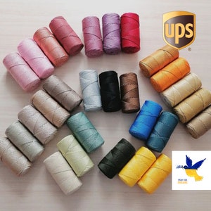 Op de afbeelding: Assortiment van 20 spoelen met gekleurde gewaxt katoenen koord. De koorden zijn in een cirkel op een licht houten oppervlak gerangschikt. De koorden zijn in verschillende kleuren, waaronder roze, rood, oranje, geel, groen, blauw, paars, bruin en zwart.