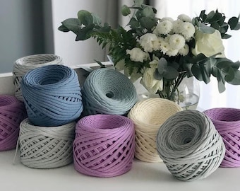 May include: A collection of eight balls of yarn in various shades of blue, gray, purple, and cream. The yarn is made of a thick, textured material and is perfect for crocheting or knitting.
