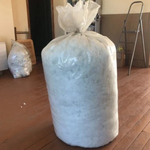 May include: A large clear plastic bag filled with white packing peanuts. The bag is sitting on a wooden floor.