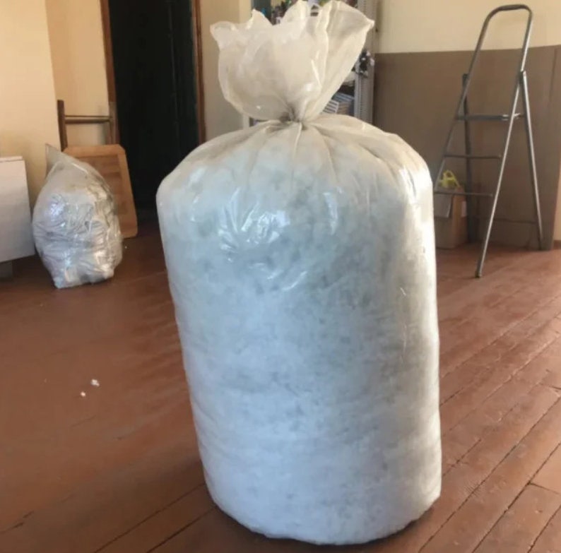 May include: A large clear plastic bag filled with white packing peanuts. The bag is sitting on a wooden floor.