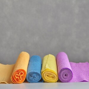 Pu&ograve; includere: Cinque rotoli di carta velina di diversi colori: giallo, arancione, blu, giallo e viola. I rotoli sono disposti in fila su una superficie bianca.