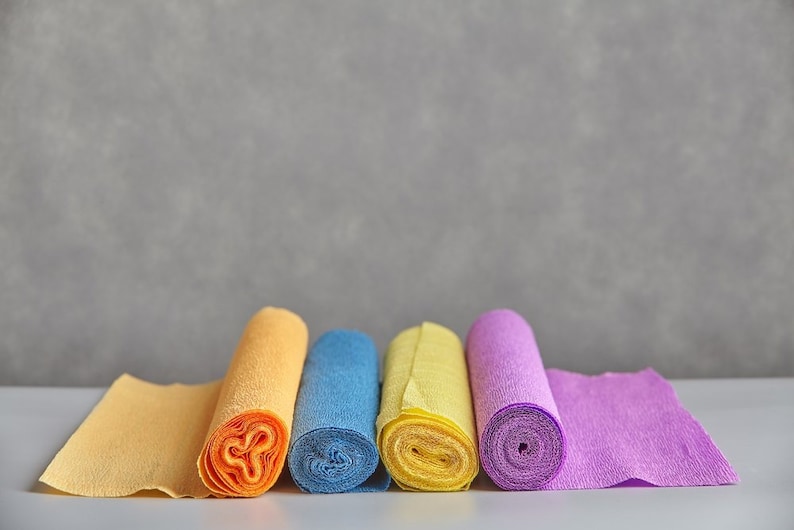 Pu&ograve; includere: Cinque rotoli di carta velina di diversi colori: giallo, arancione, blu, giallo e viola. I rotoli sono disposti in fila su una superficie bianca.