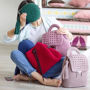 May include: A collection of four crocheted bags in different colors and styles. The bags include a round green bag, a blue bag, a red backpack, and a pink backpack. The bags are all made with a chunky yarn and have a textured look.