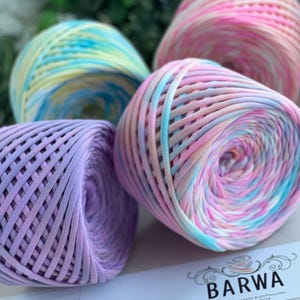 Puede incluir: Cuatro ovillos de hilo coloridos en tonos pastel de rosa, azul, amarillo y morado. El hilo está bien enrollado, mostrando una textura tejida. La imagen incluye una etiqueta con la marca "BARWA" y el texto "yarn made in Ukraine."