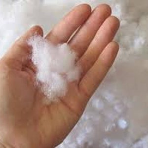 May include: A close-up of a handful of white polyester fiberfill, a soft and fluffy material used for stuffing pillows, cushions, and other plush items.