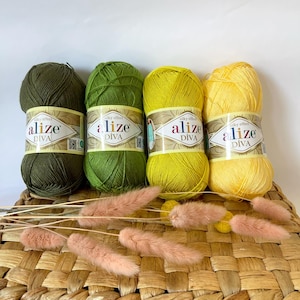Peut inclure: Quatre pelotes de fil Alize Diva, aux couleurs vert et jaune, avec un effet soyeux. Le fil est présenté sur un panier tressé avec des fleurs séchées roses.
