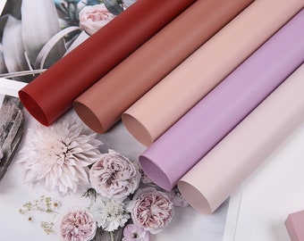 Könnte beinhalten: Fünf Rollen Seidenpapier in verschiedenen Schattierungen von Rosa, Rot und Lila. Die Rollen sind fächerförmig angeordnet, wobei die dunkelste Farbe oben und die hellste Farbe unten ist.