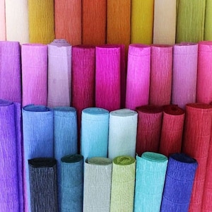 May include: A collection of numerous rolls of crepe paper arranged in a dense grid. The rolls display a wide spectrum of colours including shades of purple, blue, pink, red, orange, yellow, green, and white, all featuring a distinct crinkled texture.