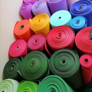 May include: A collection of colorful rolls of craft foam in various shades, including orange, yellow, pink, red, green, blue, and purple. The rolls are tightly wound, showcasing the texture and thickness of the material. The image is well-lit, highlighting the vibrant colors.