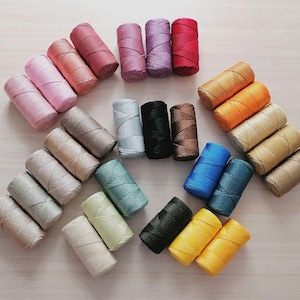 May include: A selection of colourful thread spools in shades of pink, red, blue, green, yellow, and brown. The spools are arranged to display the range of colours. Suitable for crafting and sewing projects.